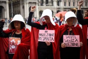 Tre donne vestite come in The handmaid´s tale con cuffia bianca e mantello rosso durante proteste contro gli obiettori di coscienza a Milano