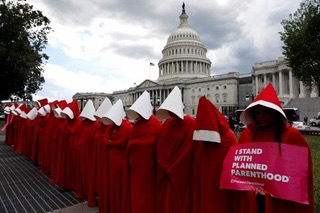 Gruppo di donne in riga vestite come in The handmaid´s tale con mantello rosso e cuffia bianca d´avanti a Capitol Hill